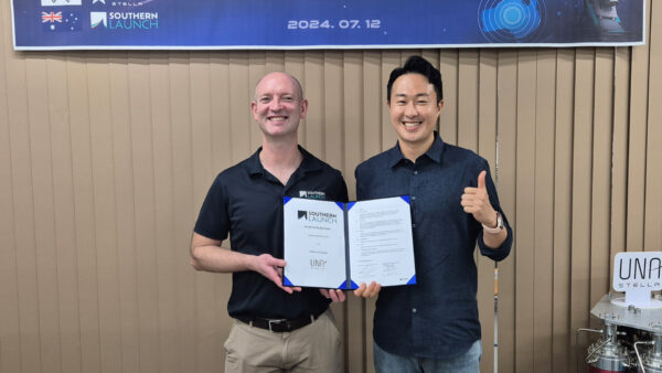 Two men at a launch facility holding a signed agreement