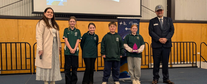 Two guest judges and four school kids from Riverdale Primary School standing on stage accepting an award for the 2025 Kids in Space program final.