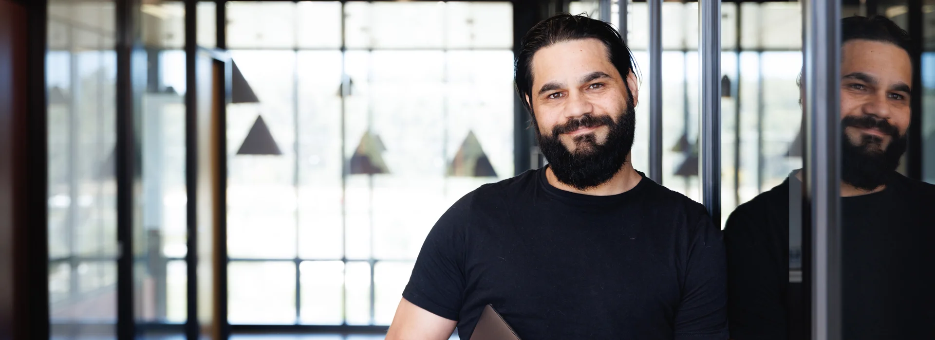 Aboriginal Intern smiling, wearing a black T-shirt and holding a closed laptop