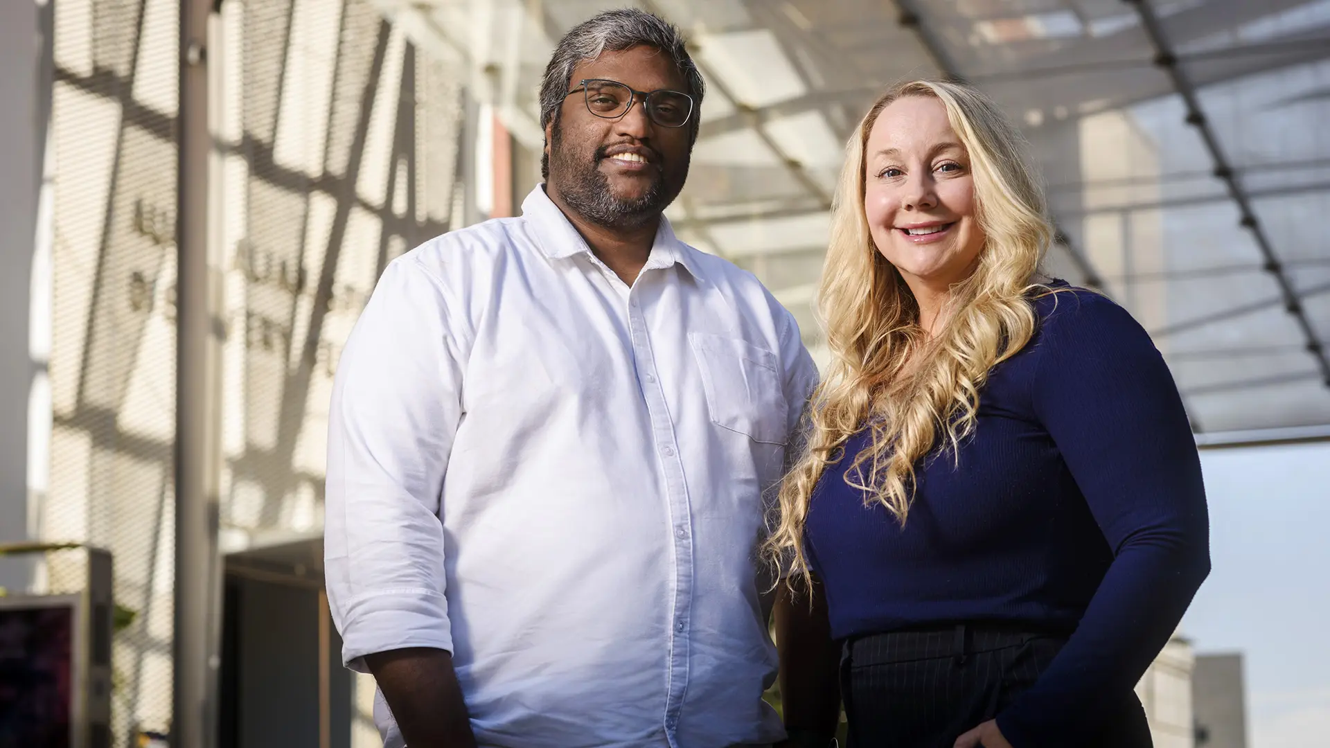 A man and woman stand together in front of an abstract, modern-looking building
