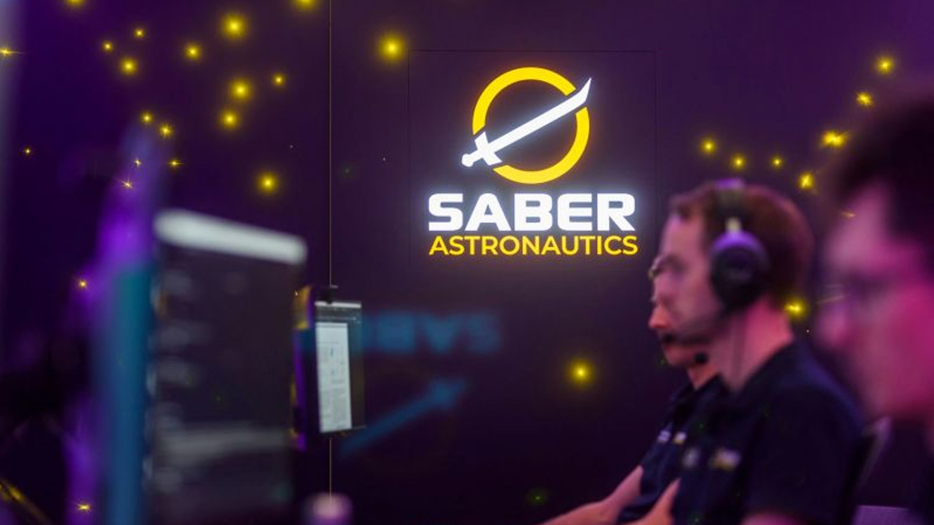 Saber Astronautics Three people sitting at their computers in a dark themed room