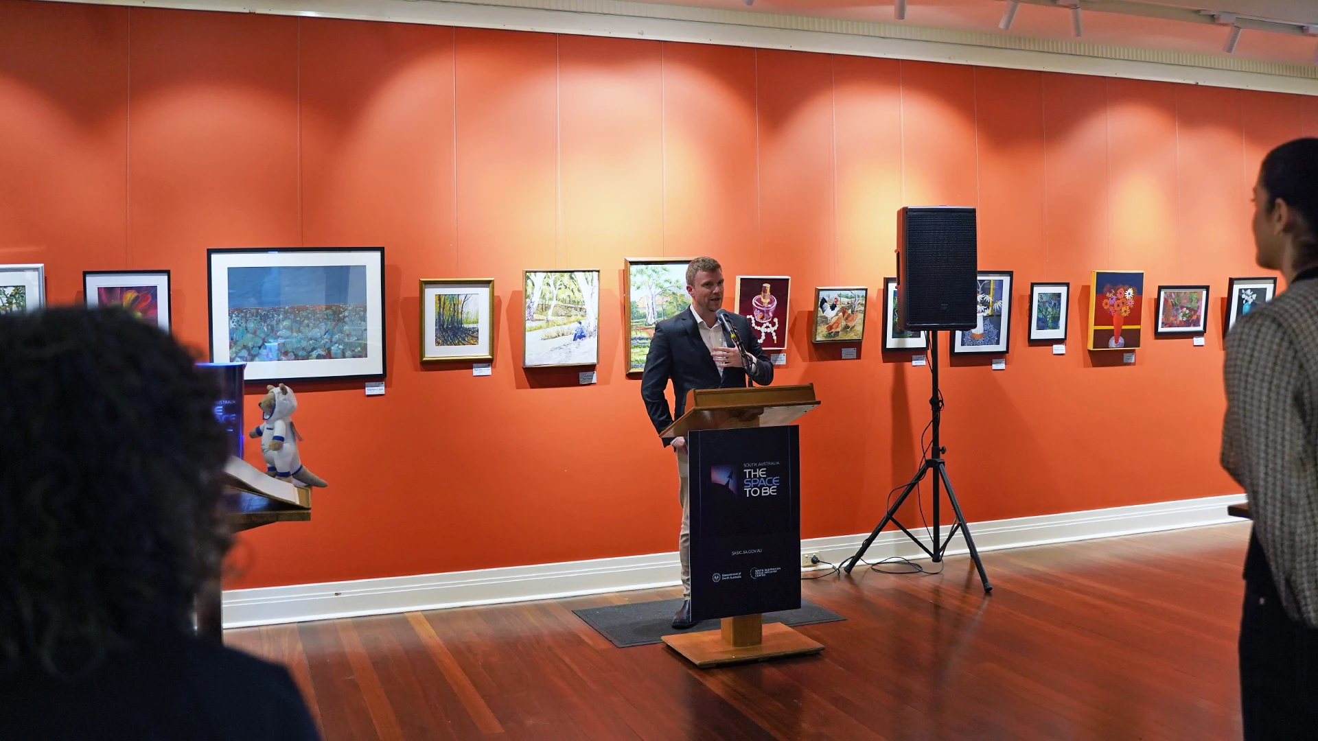 SASIC Regional Engagement Program Corporate man standing in front of a orange wall with pictures speaking to a large room full of people