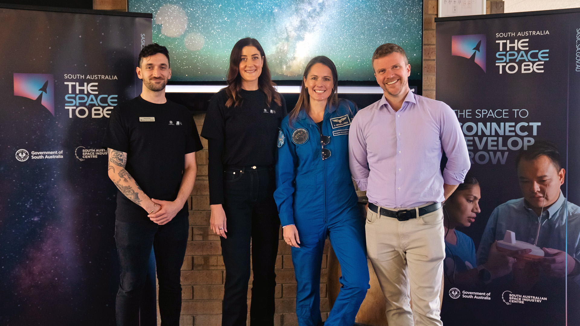 Four people standing together in front of two space branded banners at an event