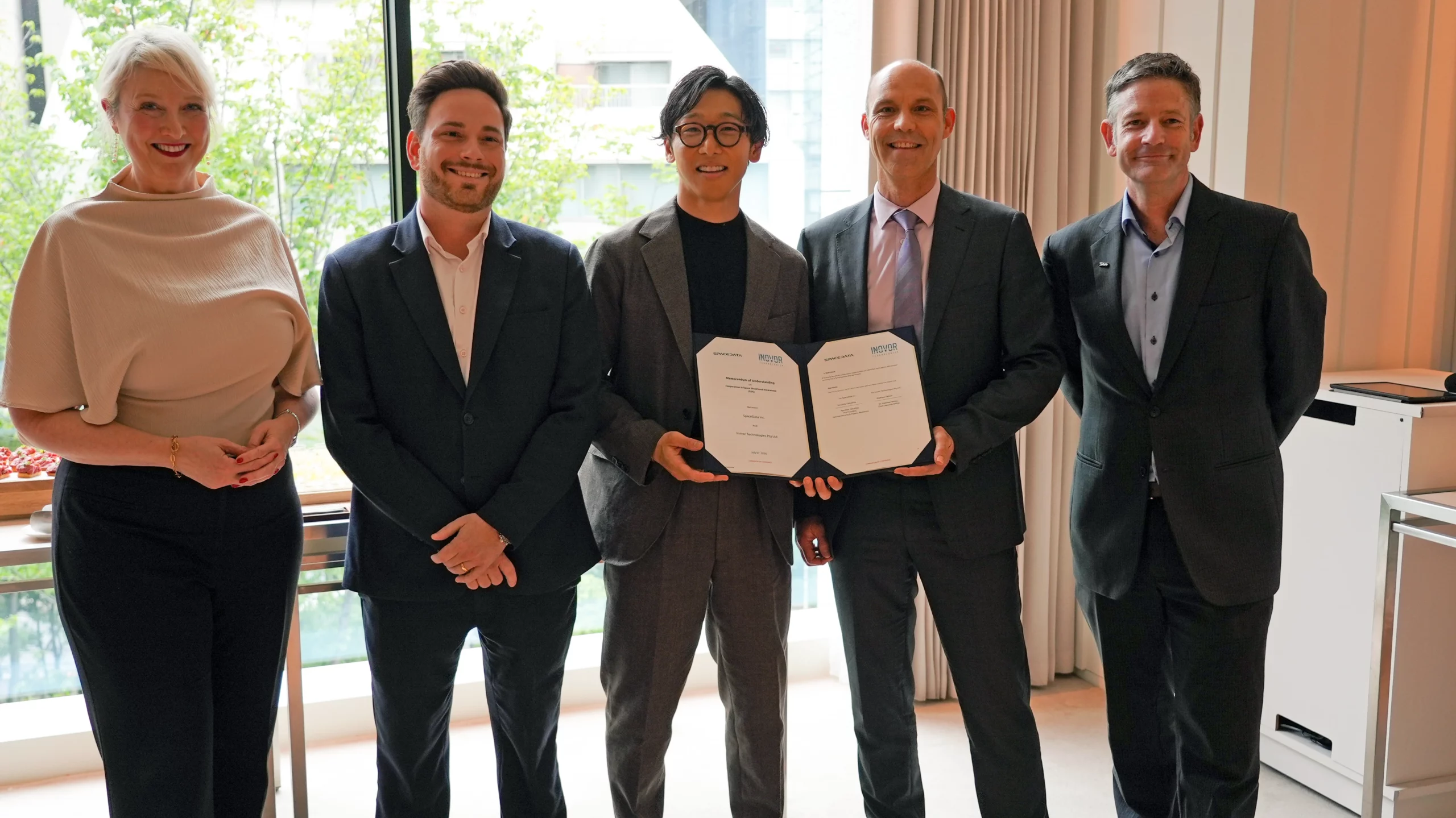 A group of people standing in front of a window holding a partnership agreement