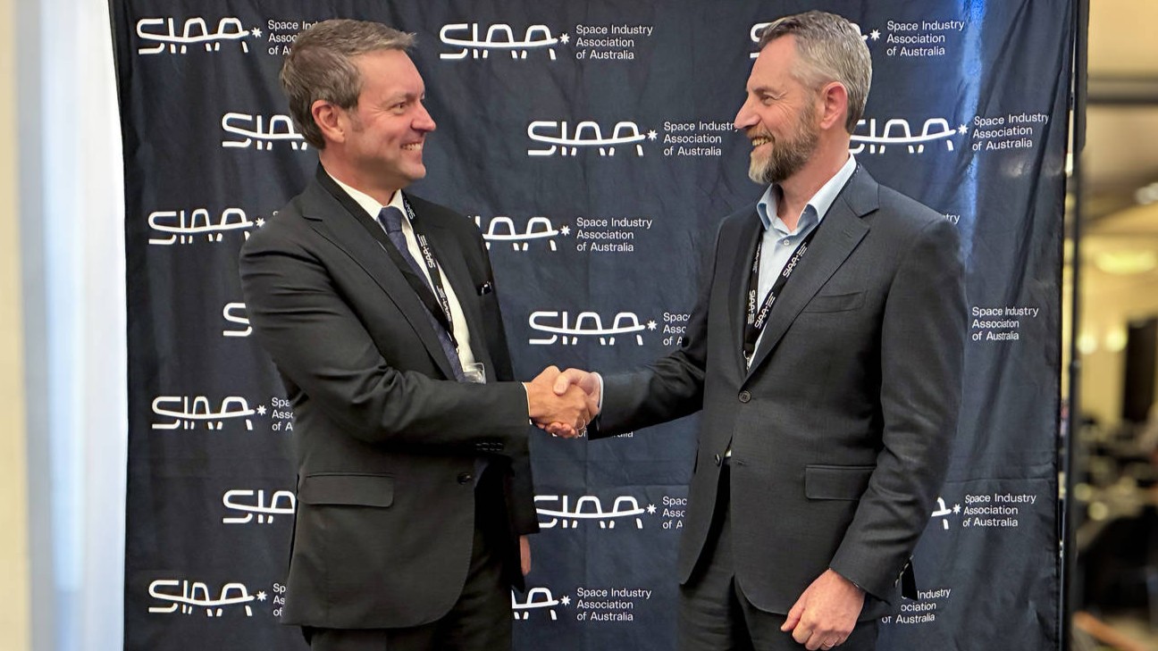 Two people shaking hands, standing in front of Space Industry Association of Australia banner.