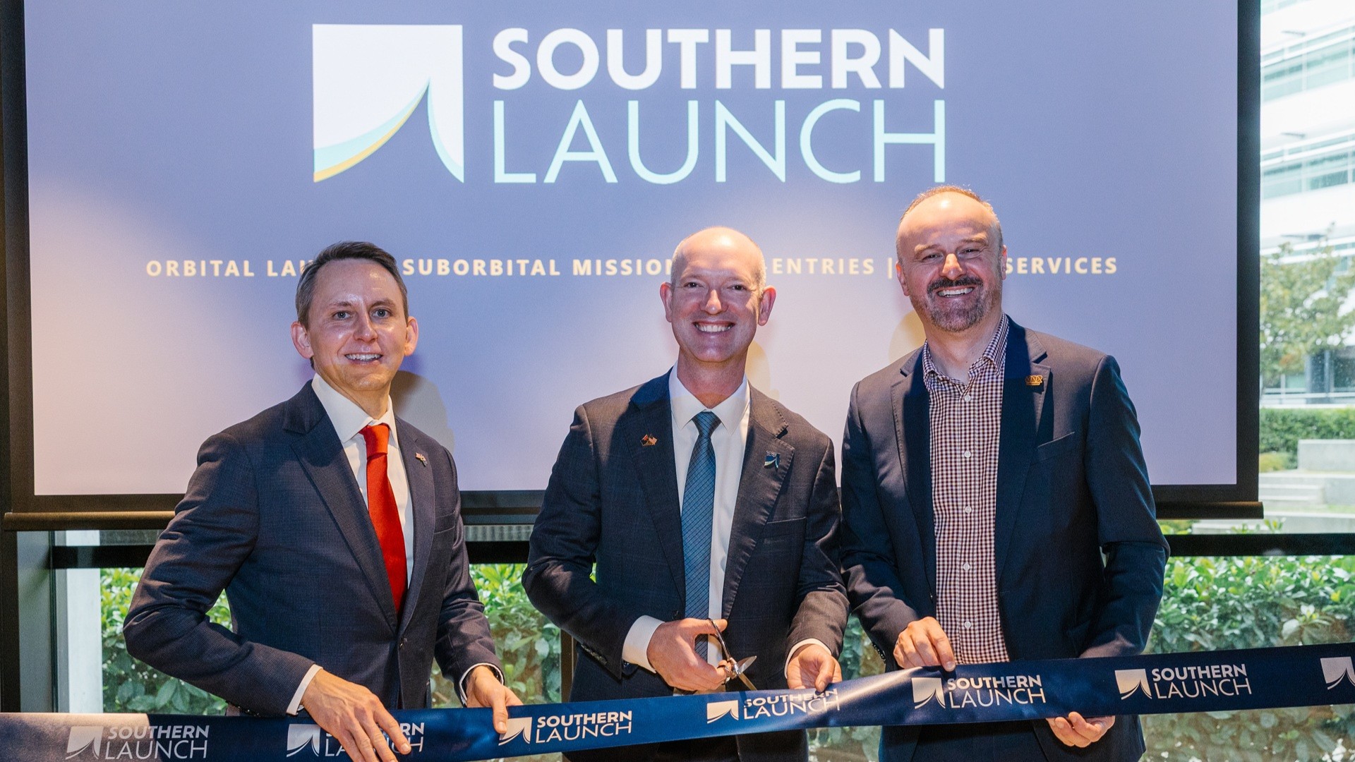 Three people cutting a ribbon to mark the opening of a new office in Canberra